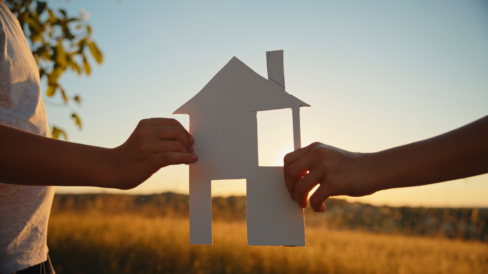 Boy And Girl Hold A House Model In A Grassy Field As The Sun Sets