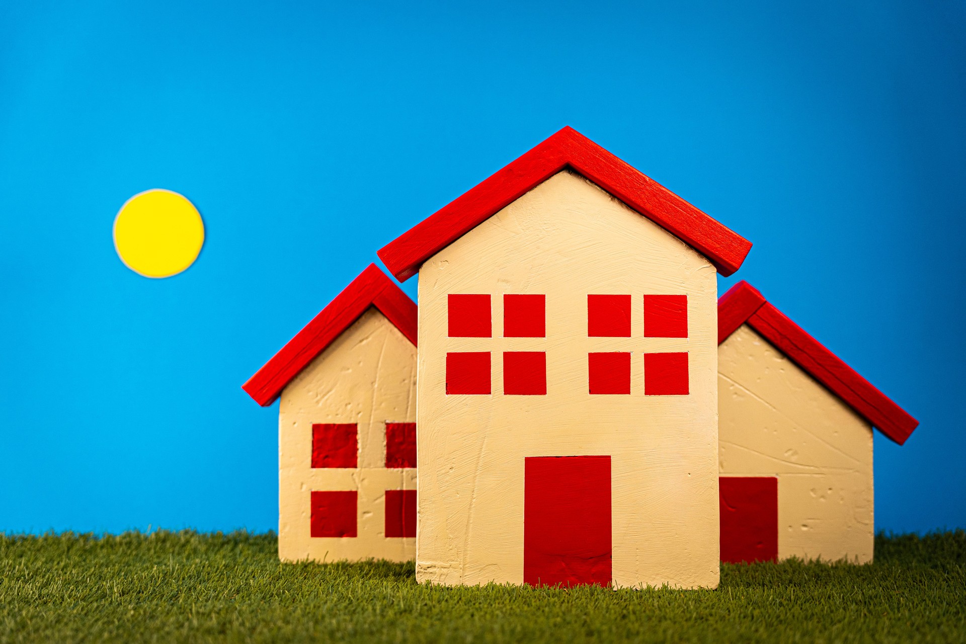 Miniature wooden houses resting on lush grass, sunlit backdrop symbolizing property investment and home ownership
